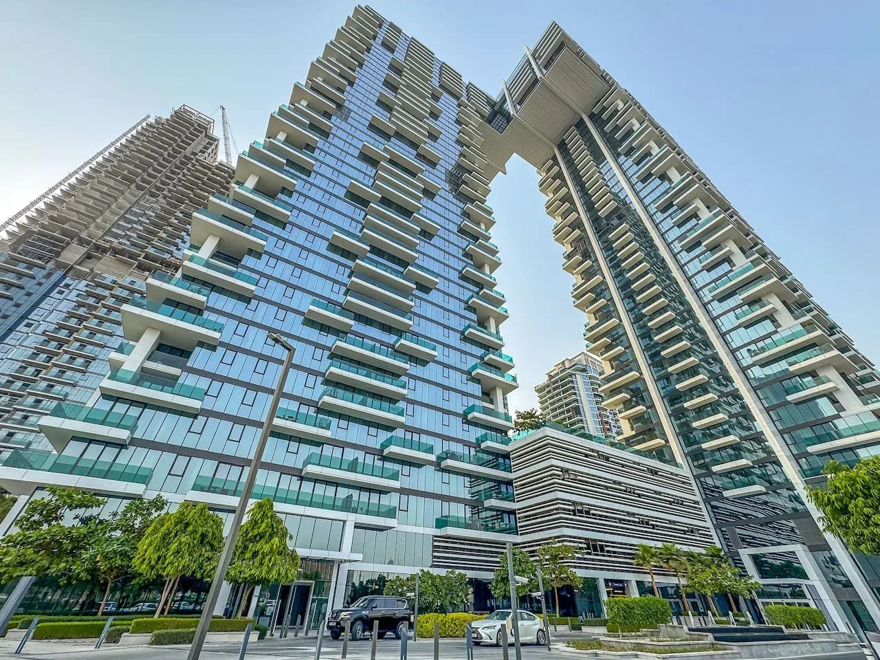 Modern high-rise buildings with glass facades and balconies rise above a landscaped entrance.