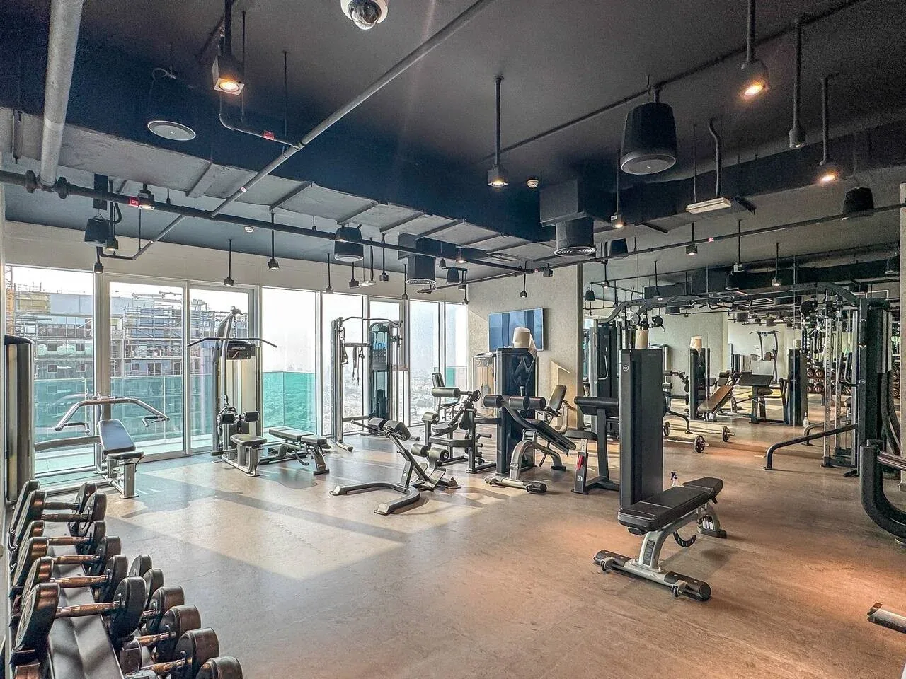 A gym with weight machines, free weights, and large windows.