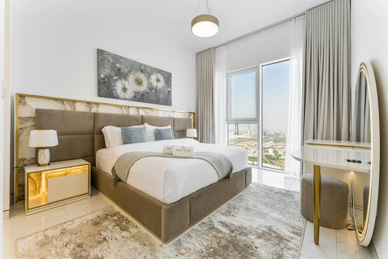 A bedroom with a neatly made bed beside a large window and floor-length curtains.