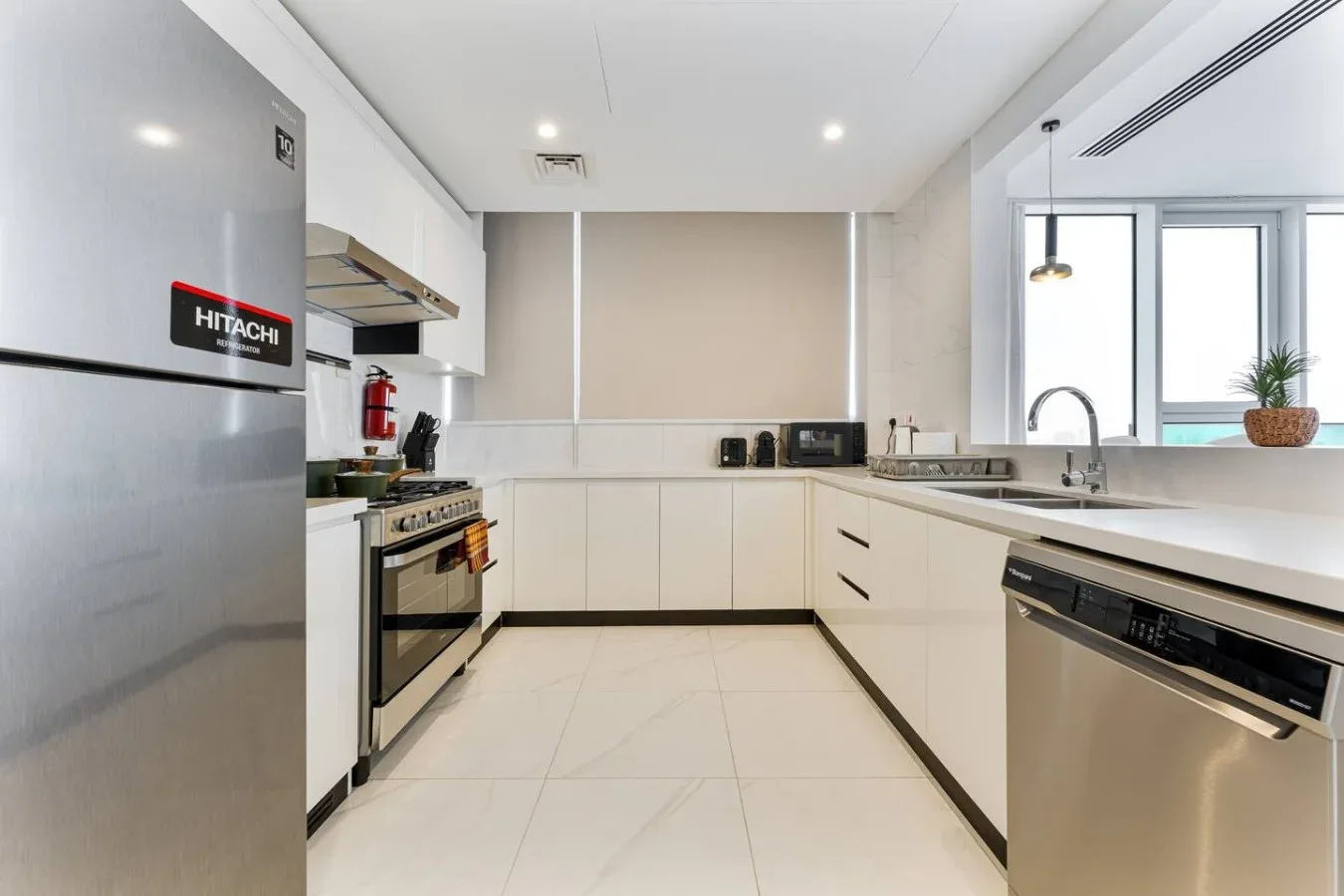 A bright modern kitchen with white cabinets, stainless steel appliances, and a large window.