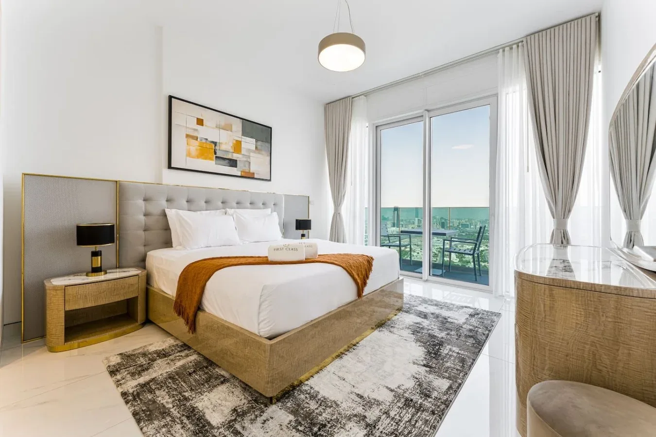 A bright bedroom features a bed beside floor-to-ceiling windows and a city view.