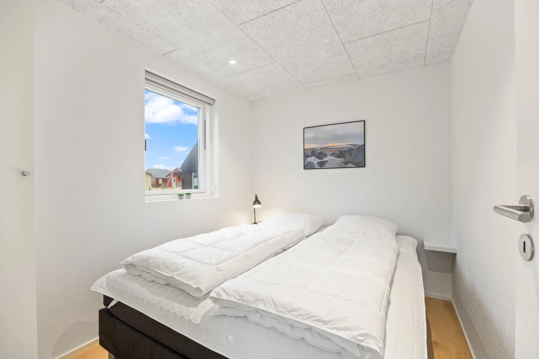 Un dormitorio luminoso con dos camas individuales, una ventana y un cuadro en la pared.