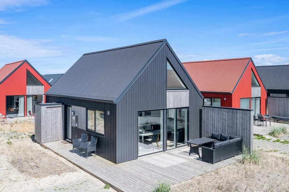 Una casa moderna de revestimiento oscuro con terraza de madera y asientos al aire libre.