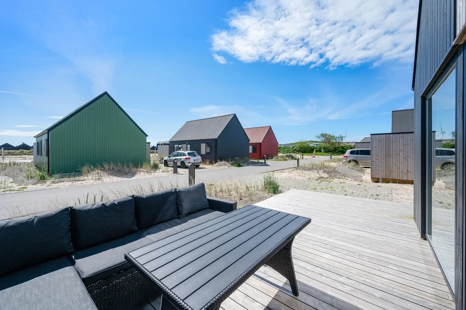 Una terraza exterior tiene asientos oscuros y una mesa baja, con pequeñas construcciones al fondo.