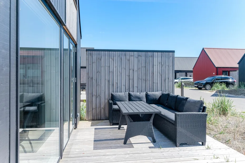 Una zona de estar al aire libre con muebles oscuros junto a una pantalla de madera.