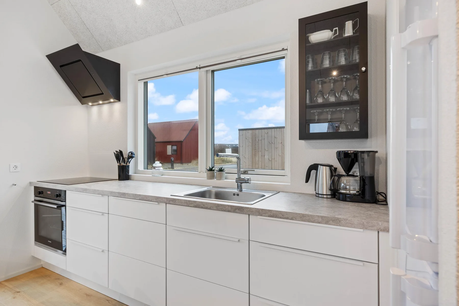 Una cocina luminosa con gabinetes blancos, un fregadero y una ventana grande.