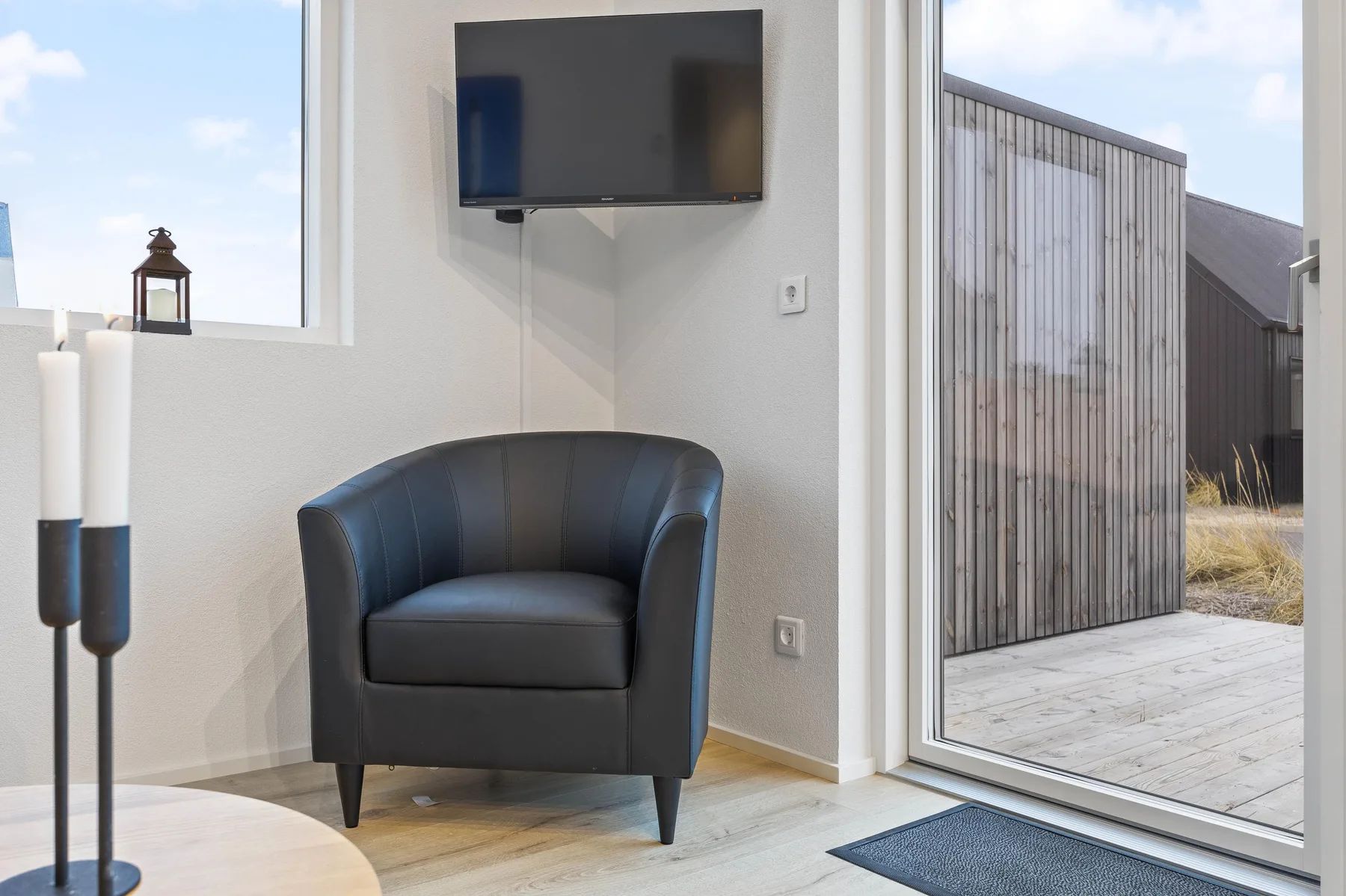 Una zona de estar con un sillón oscuro y un televisor junto a una puerta de vidrio.