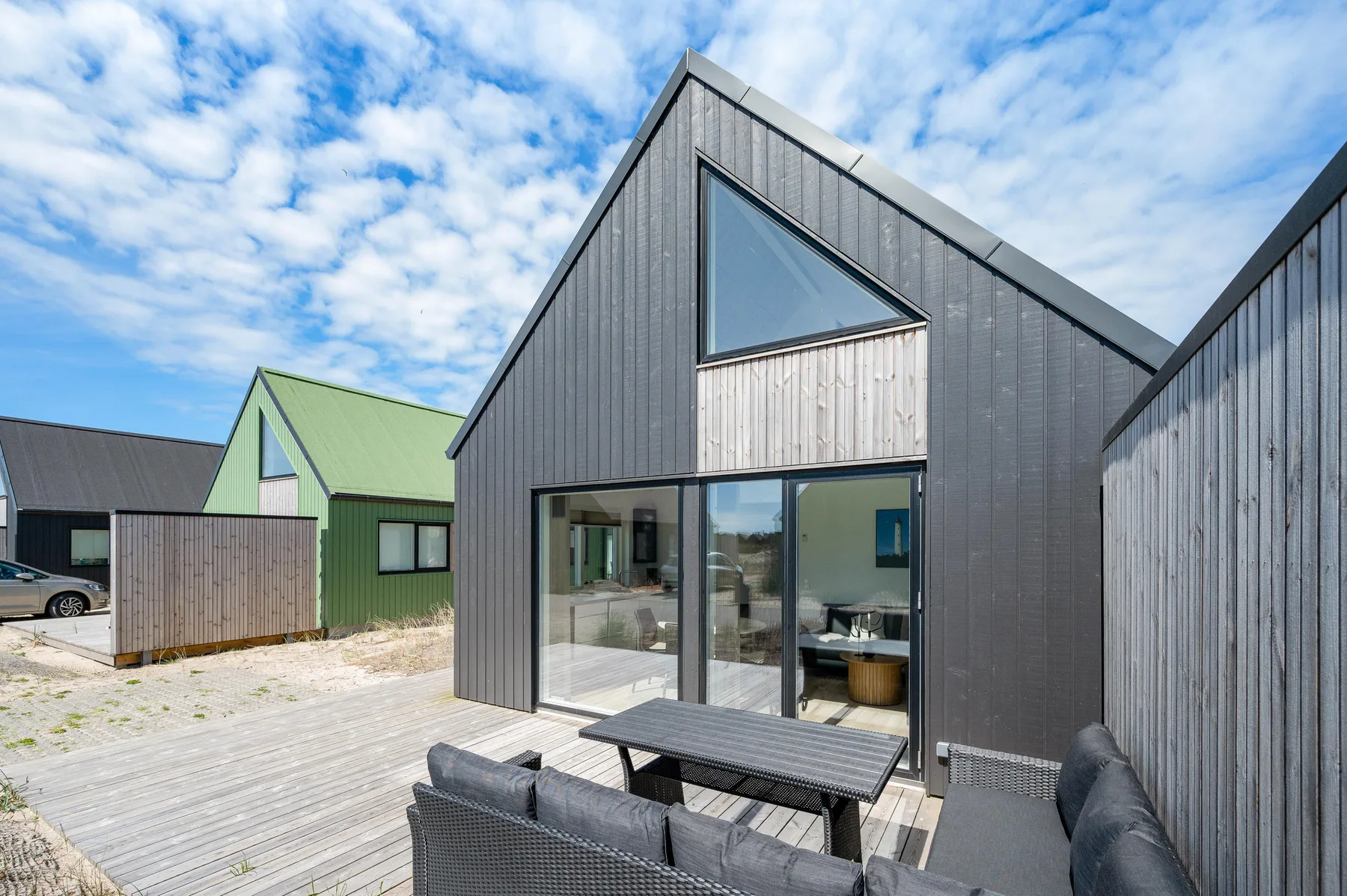 Una casa moderna se abre a una terraza de madera con asientos al aire libre.