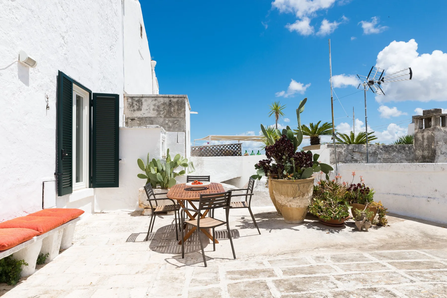 Una terraza soleada en la azotea con mesa de comedor, asientos al aire libre y plantas en macetas.
