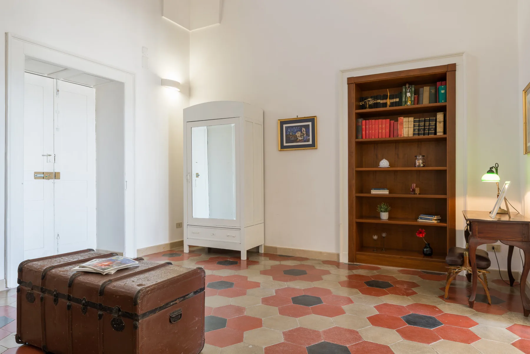 Una habitación luminosa con estantería, escritorio y suelo de baldosas.