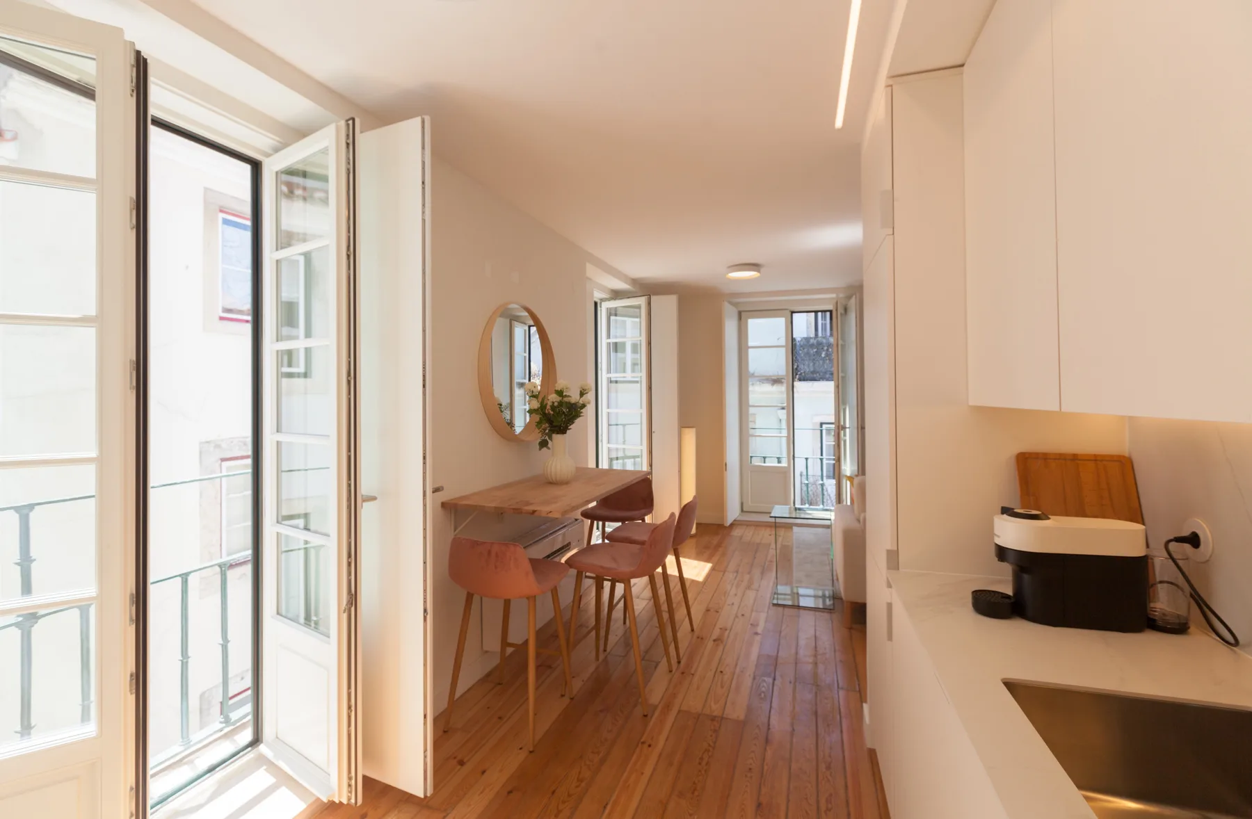 A bright apartment interior with a dining table beside tall open windows.