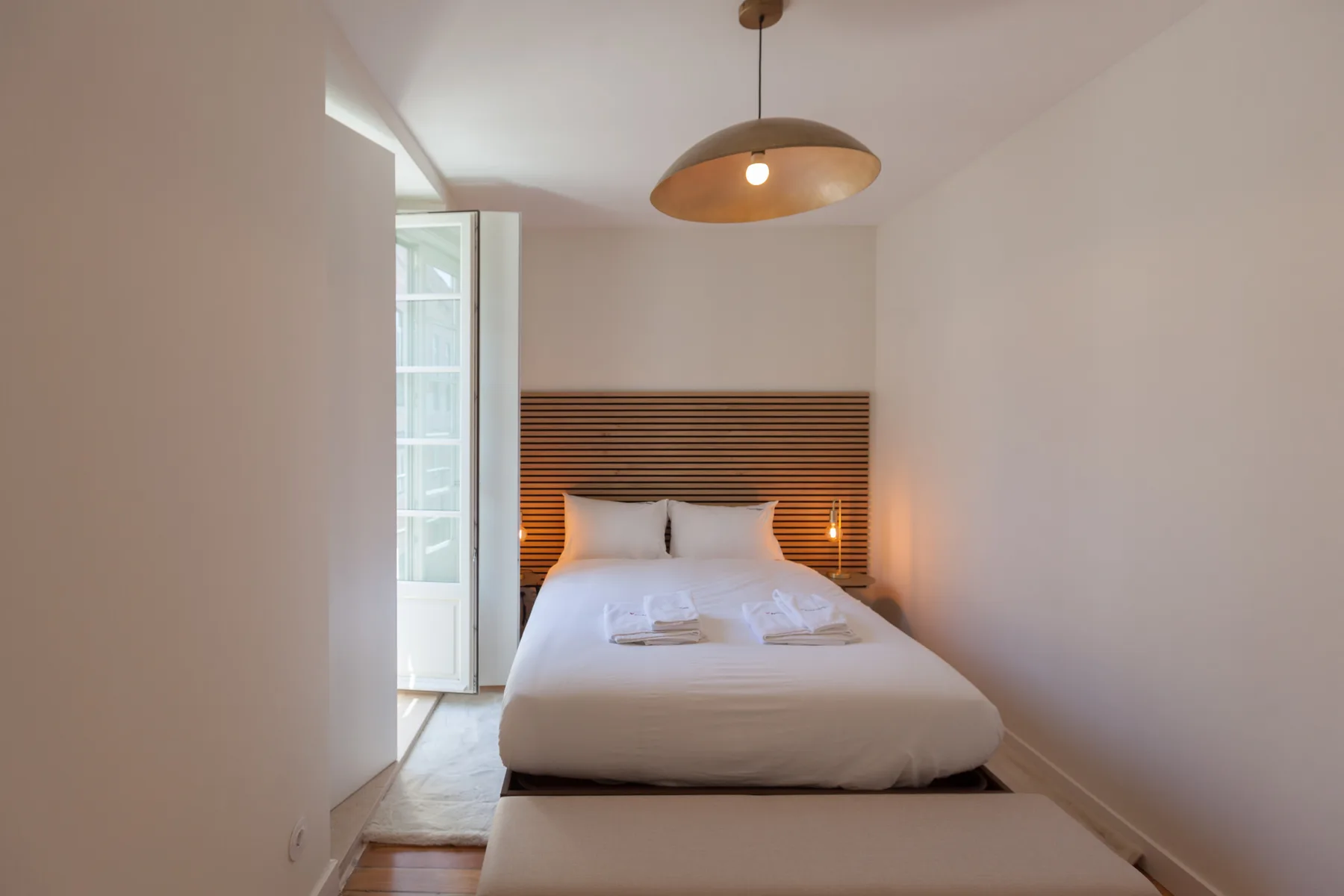 A bright bedroom with a bed beneath a striped wooden headboard.