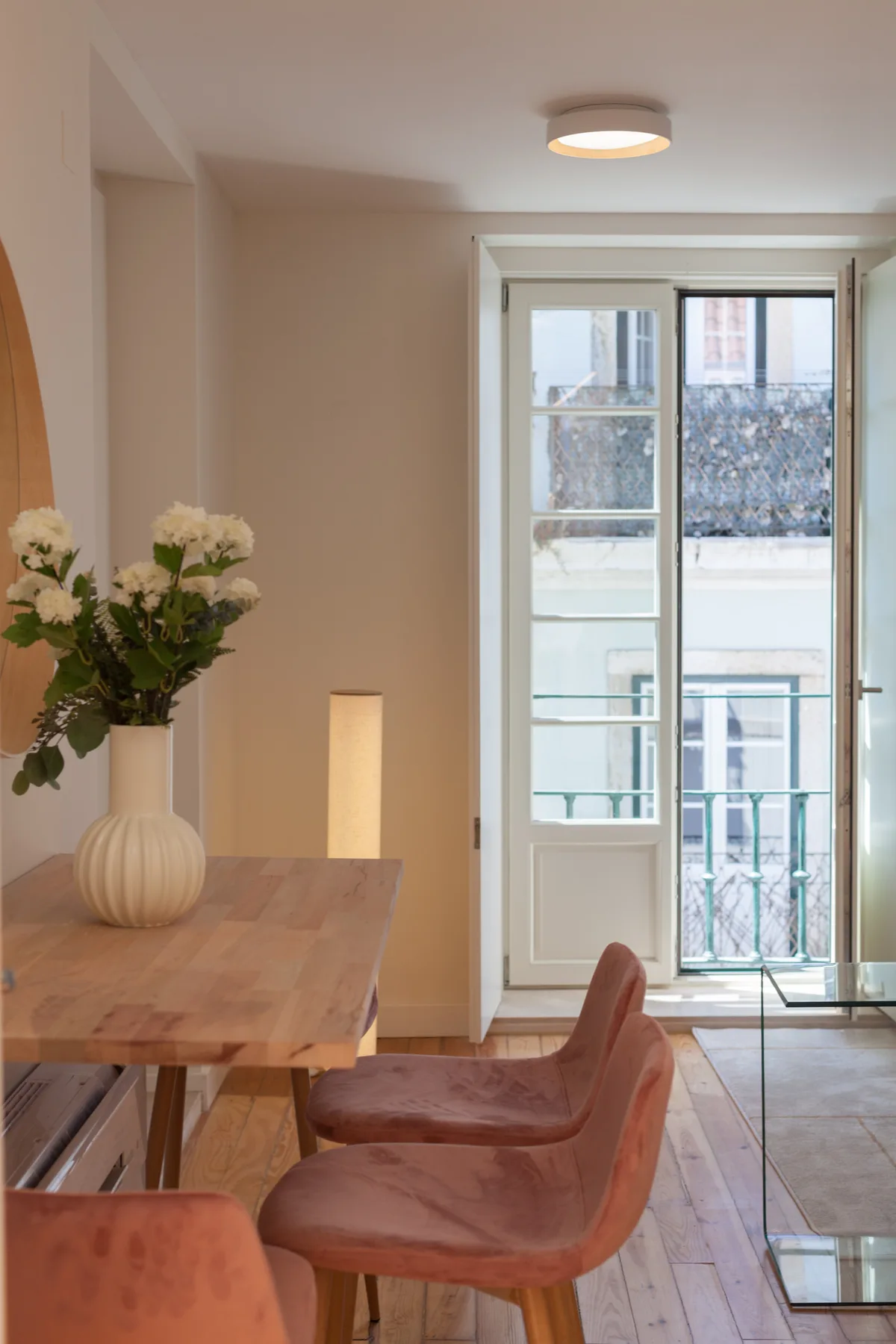A dining area with a wooden table, seating, and flowers beside glass doors.