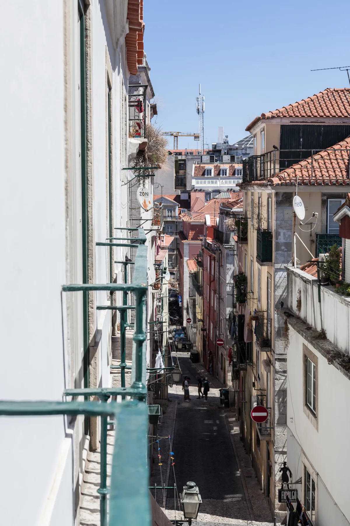 A narrow urban street runs between closely spaced buildings with balconies.