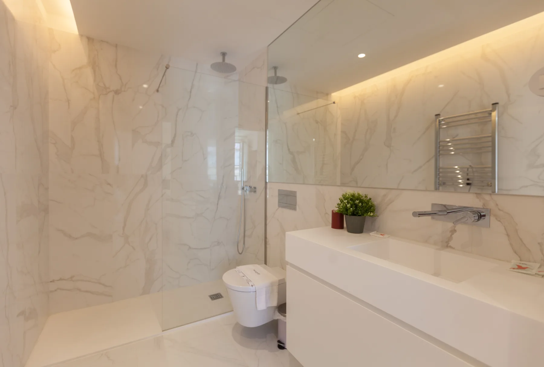 A bright bathroom with a walk-in shower, toilet, and long vanity.