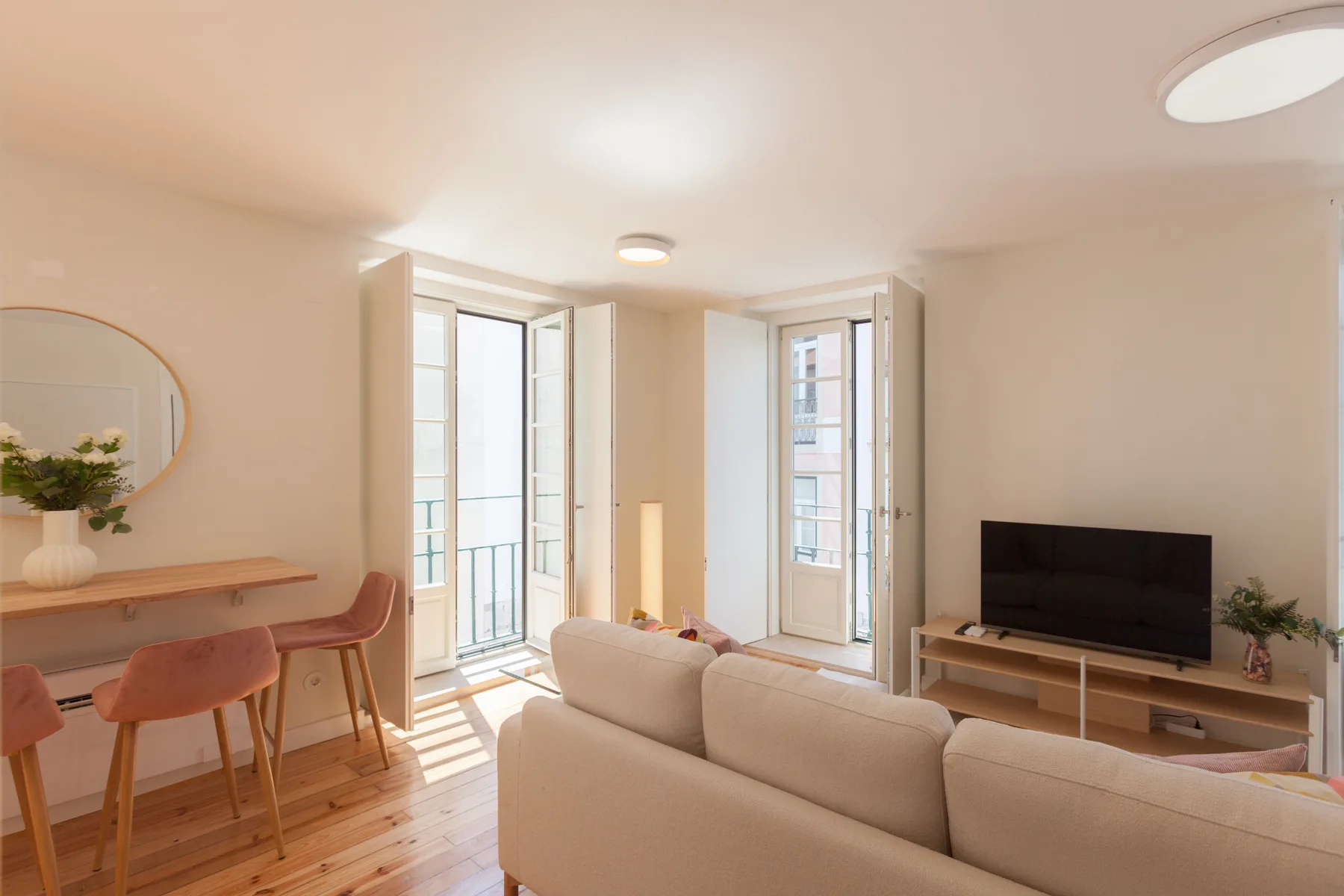 A bright living room with seating, a television, and tall windows.