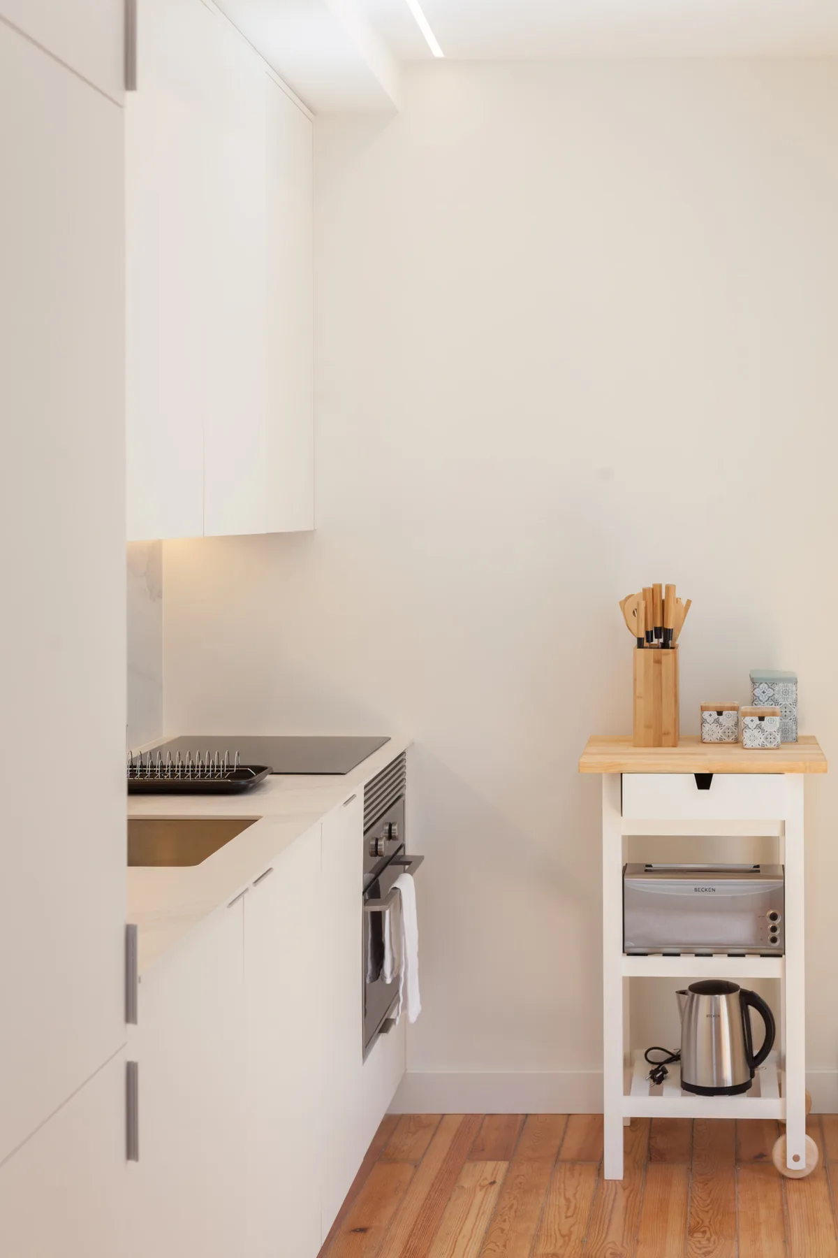A compact kitchen with white cabinetry, a cooktop, and a small storage cart.