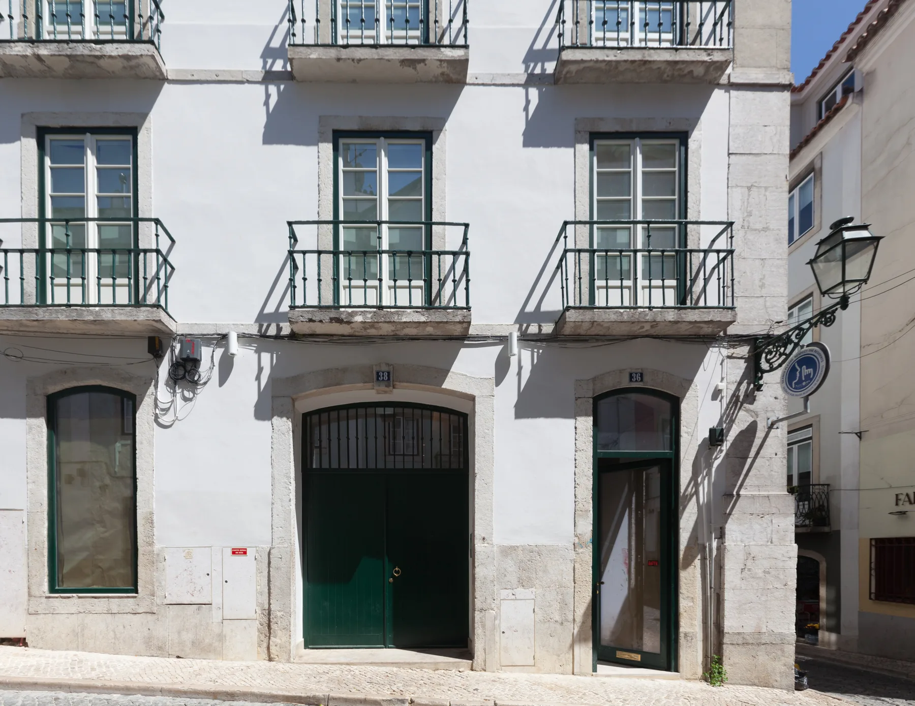 Street view of a white building with balconies above a dark green entrance.