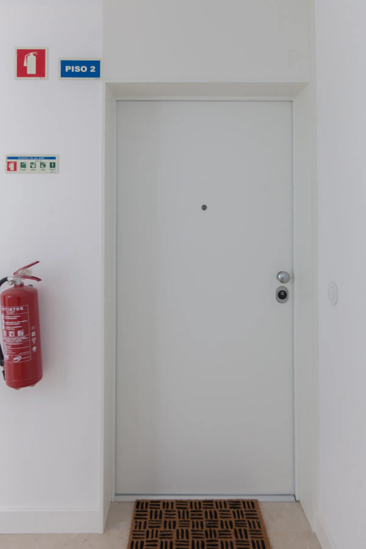 A white hallway door with a patterned mat and a fire extinguisher nearby.
