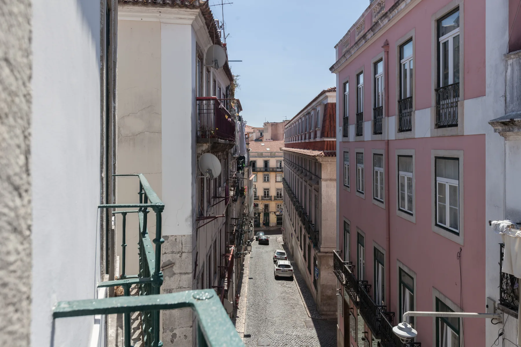 A narrow street runs between pastel-colored buildings, viewed from a balcony.