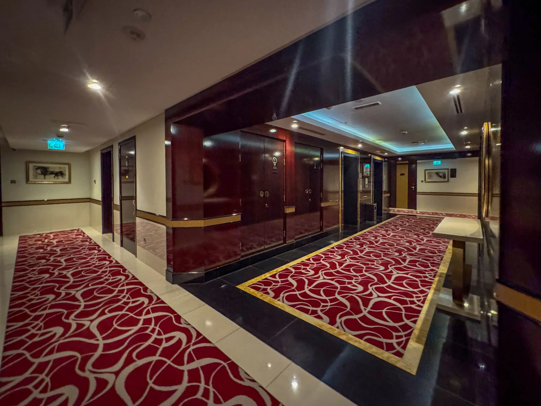 Un pasillo de hotel con alfombra roja estampada y paredes de paneles oscuros.