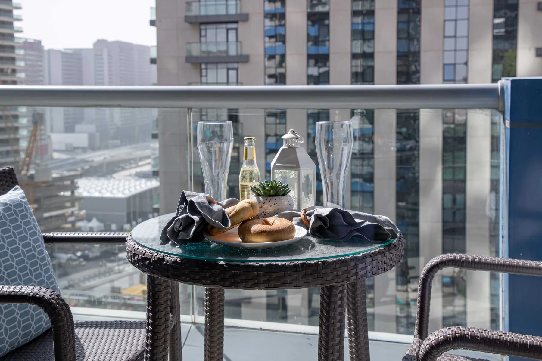 Una zona de estar en un balcón con una mesa pequeña y edificios a la vista.