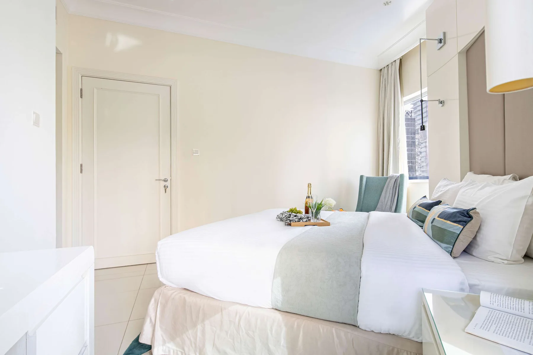 Un dormitorio luminoso con una cama bien arreglada y una pequeña bandeja encima.