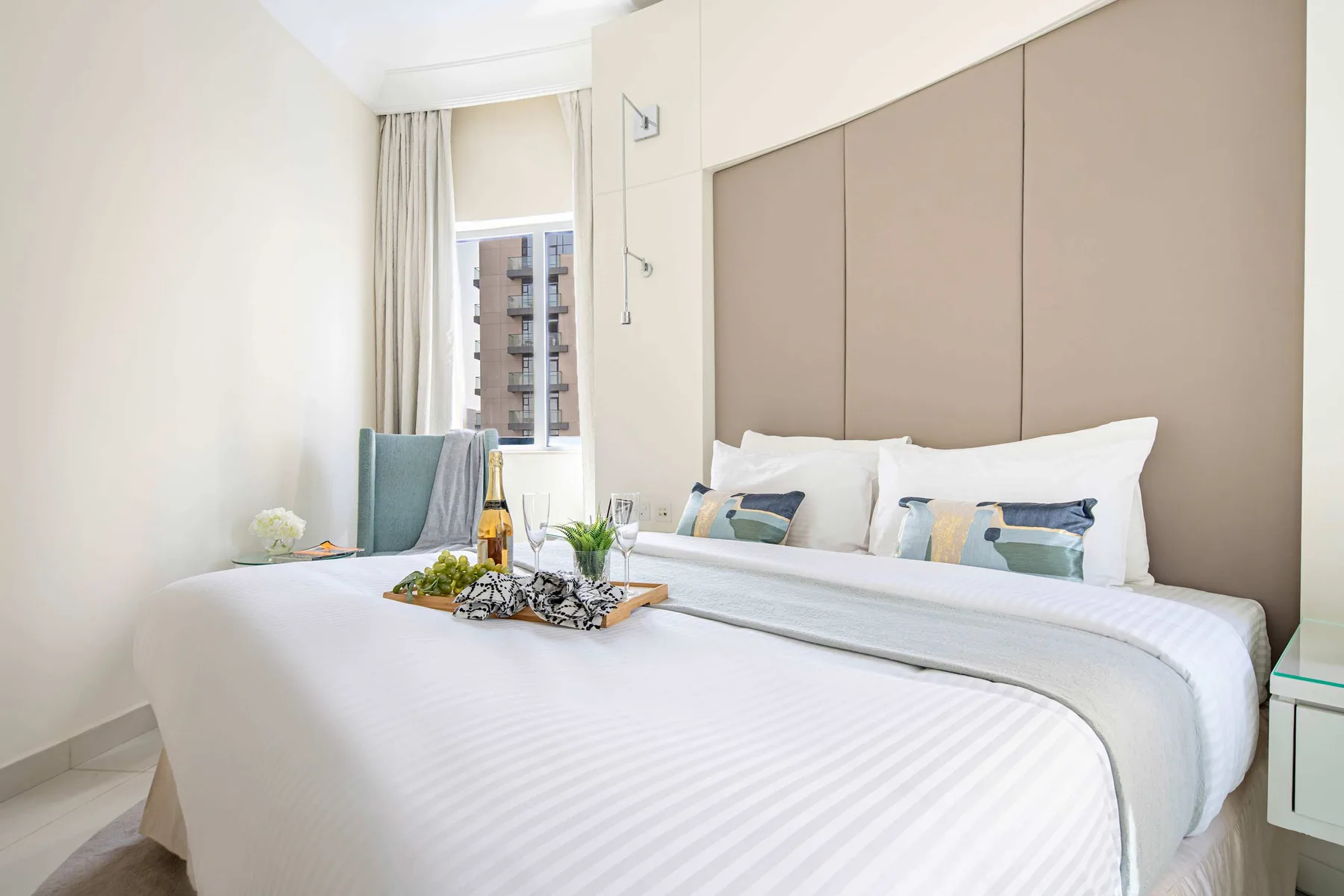 Un dormitorio luminoso con una cama bien tendida y una ventana al lado.