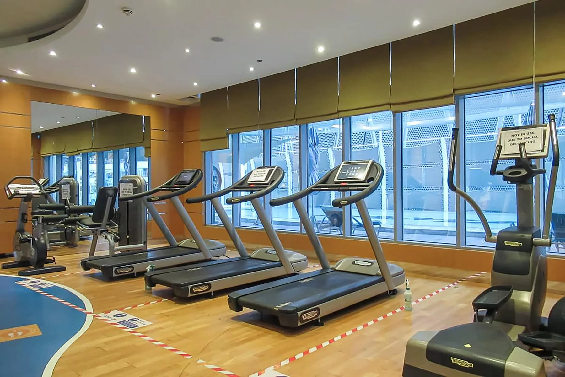 Un gimnasio con cintas de correr y equipos de ejercicio junto a grandes ventanales.