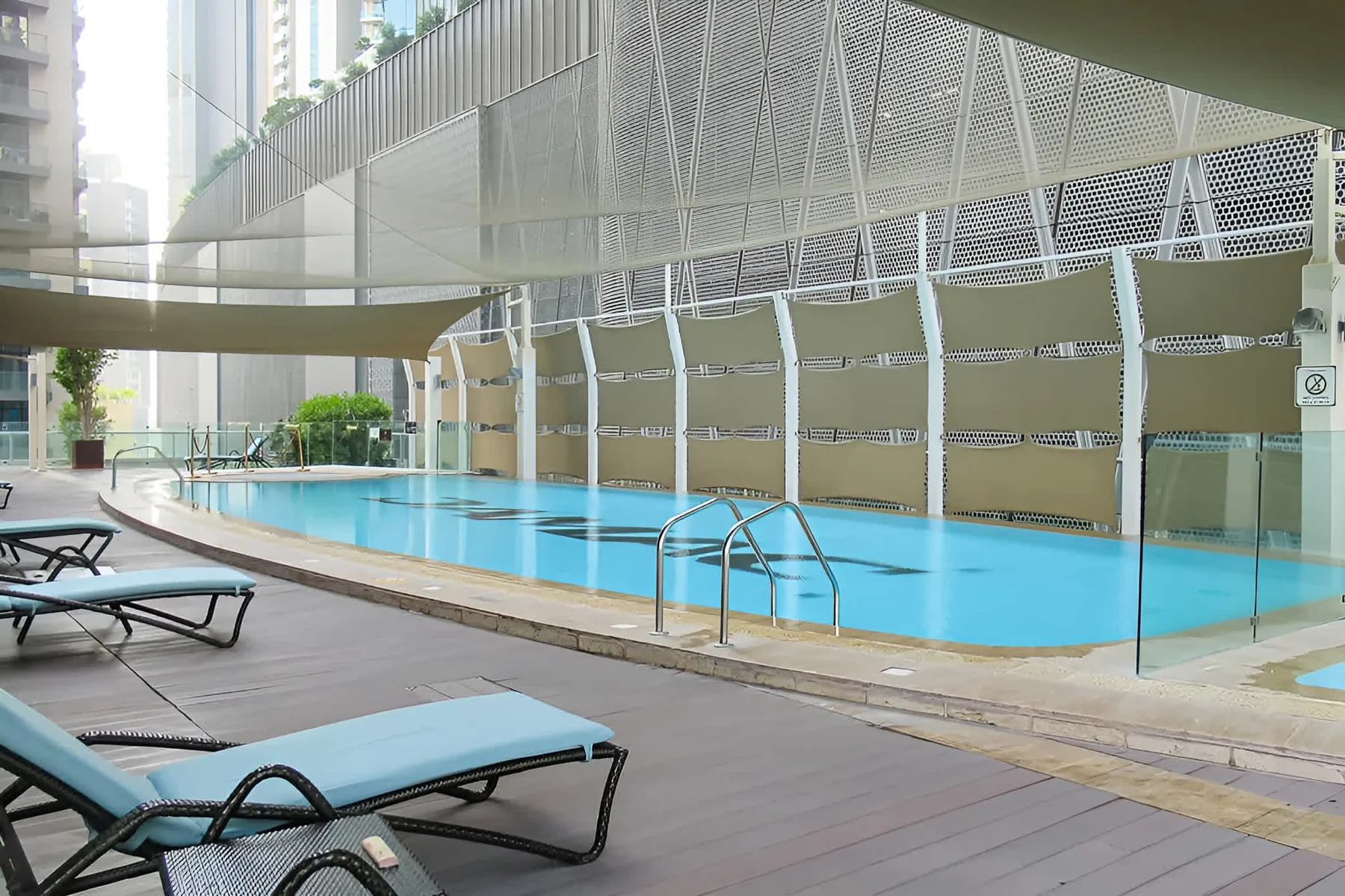Una piscina al aire libre junto a una terraza pavimentada con asientos reclinables.