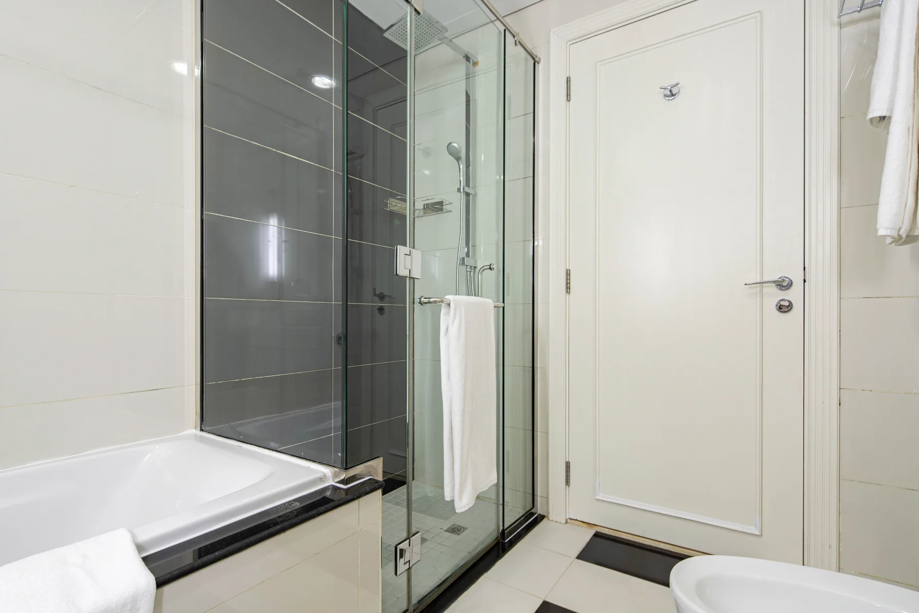 Un baño alicatado con una ducha de vidrio junto a una bañera y una puerta blanca.