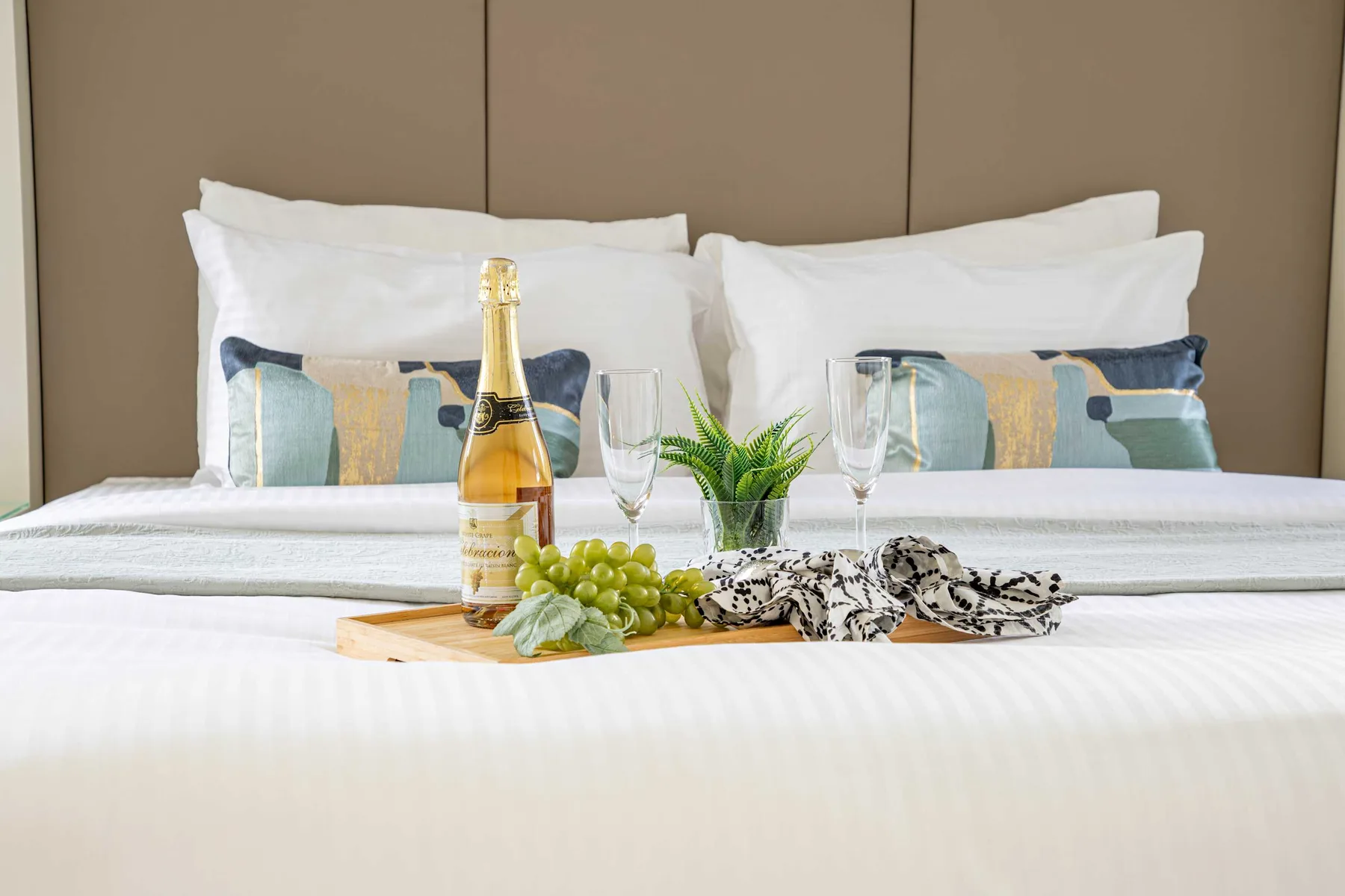 Una cama bien tendida con almohadas decorativas y una pequeña bandeja con bebidas.