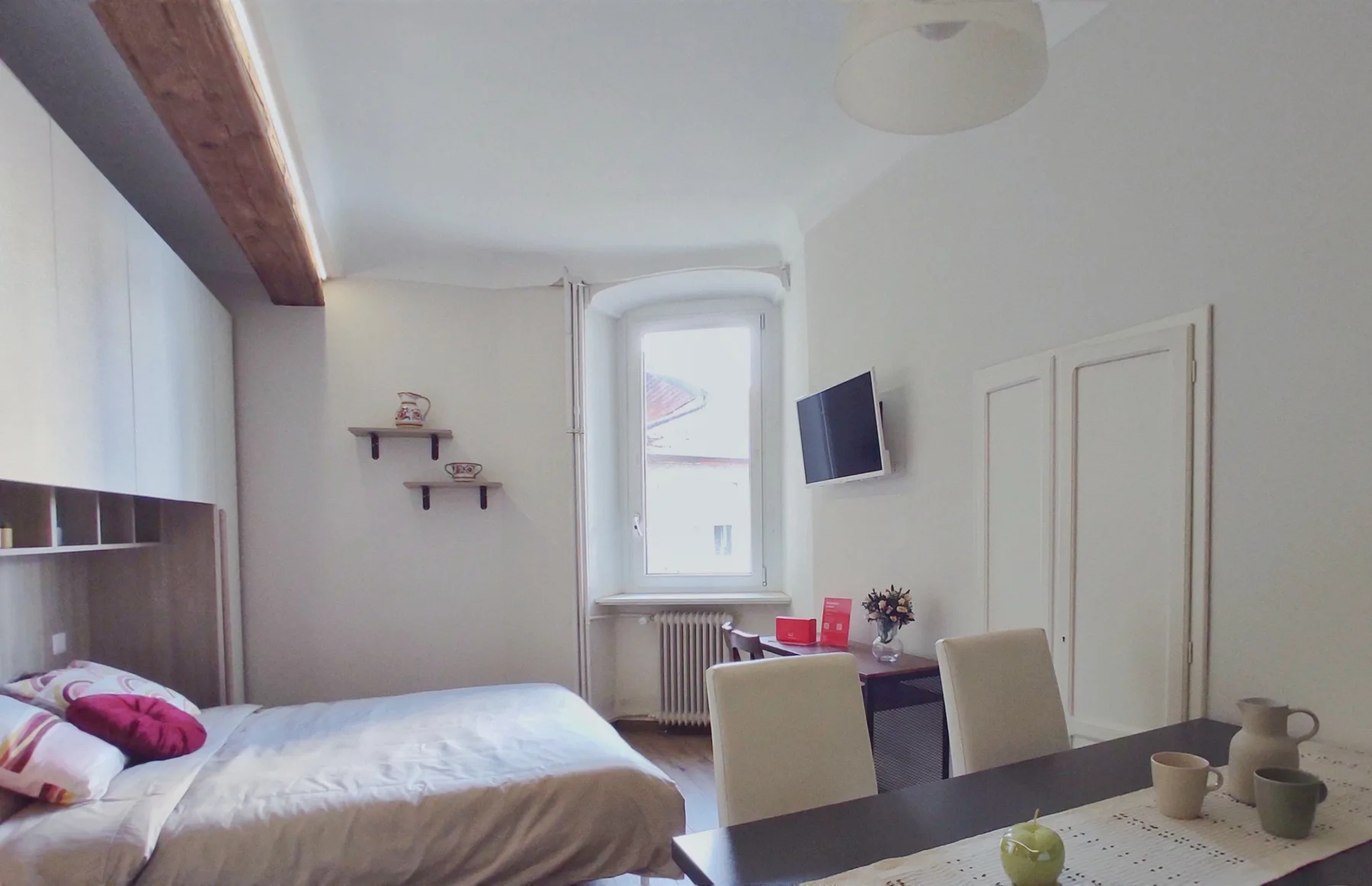 A bright bedroom with a bed, a desk, and a window.