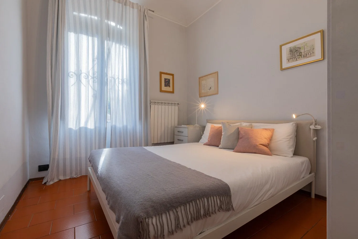 A bedroom with a neatly made bed and a tall curtained window.