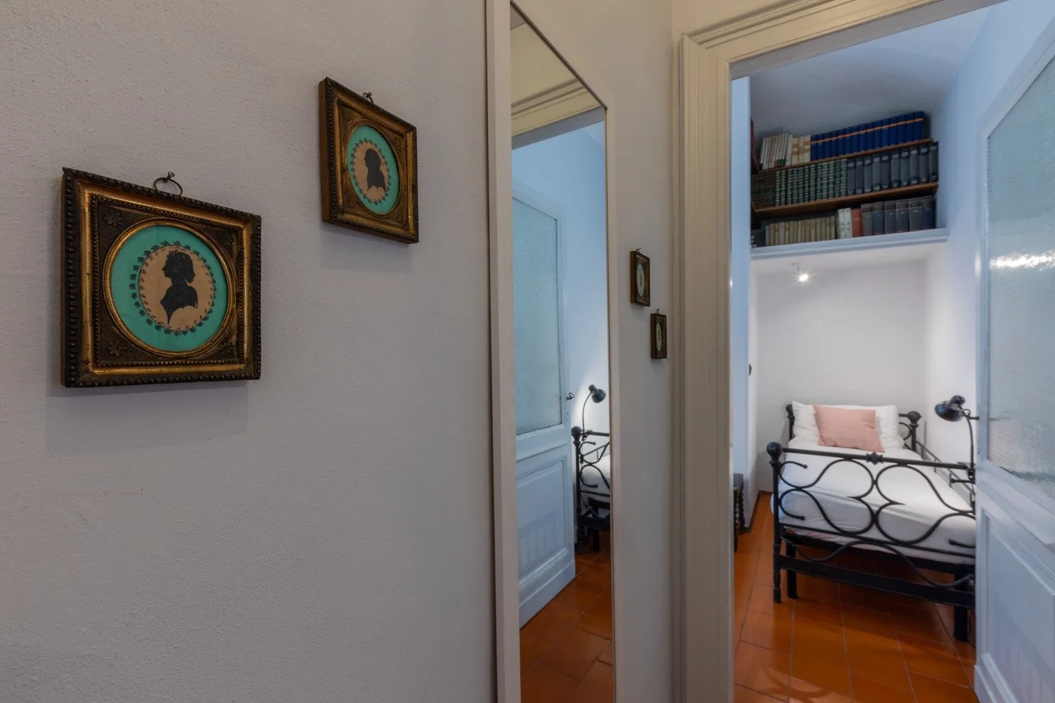 A bedroom is visible through a doorway, with a bed and bookshelves.