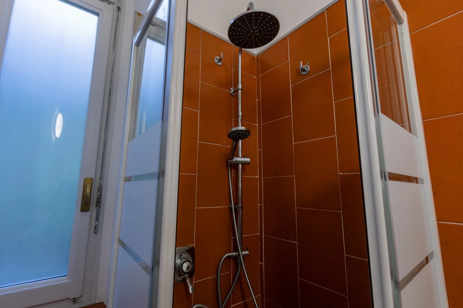 A tiled shower area with a large overhead showerhead and handheld shower.