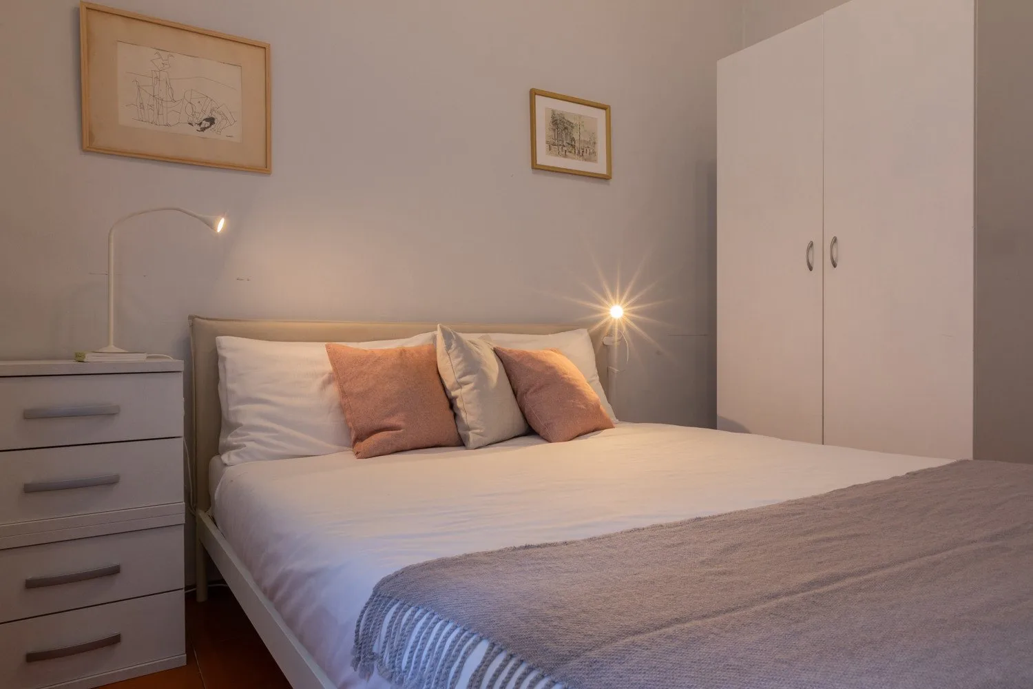 A bedroom with a neatly made bed, bedside table, and wardrobe.
