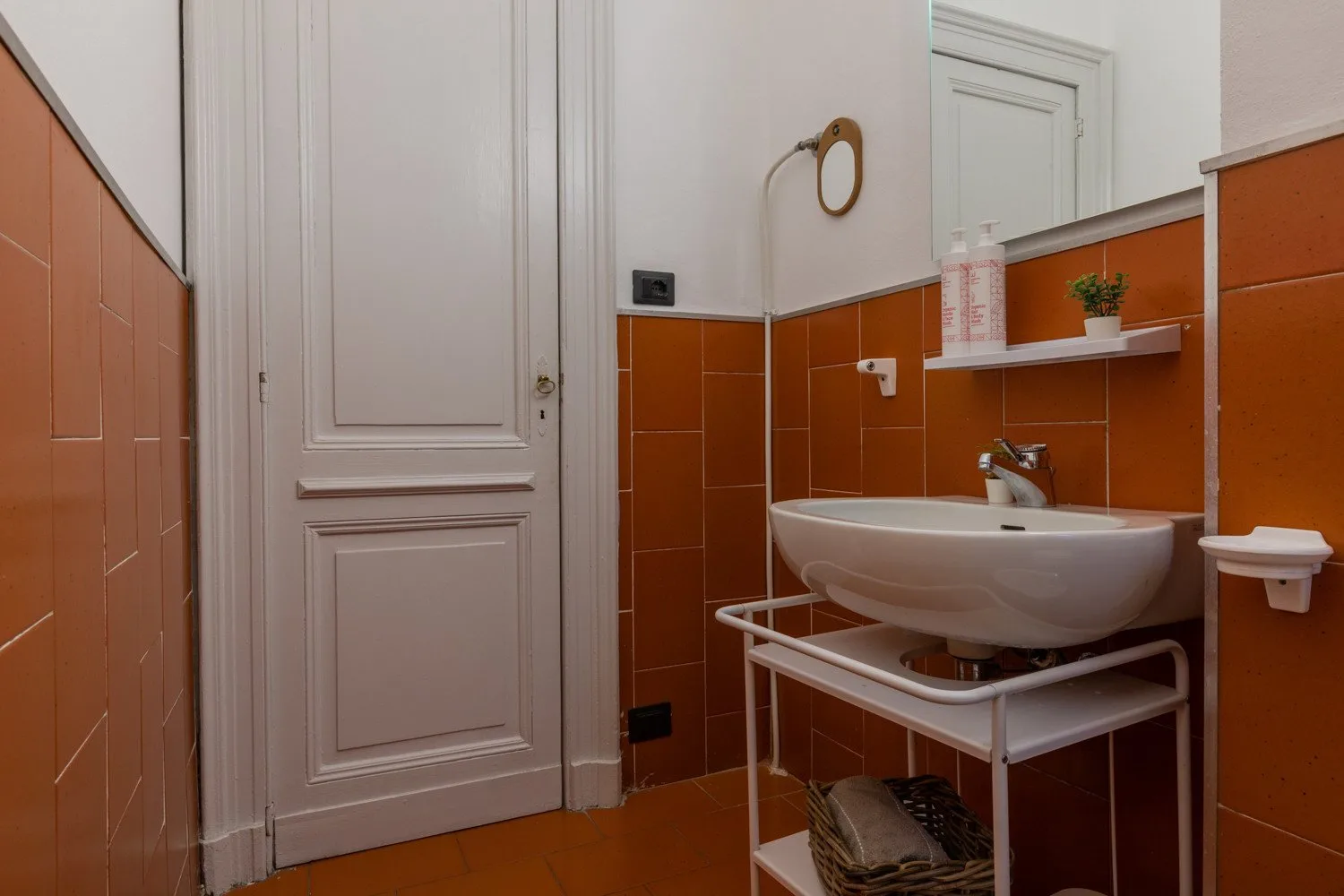 A bathroom with a white sink and orange wall tiles.
