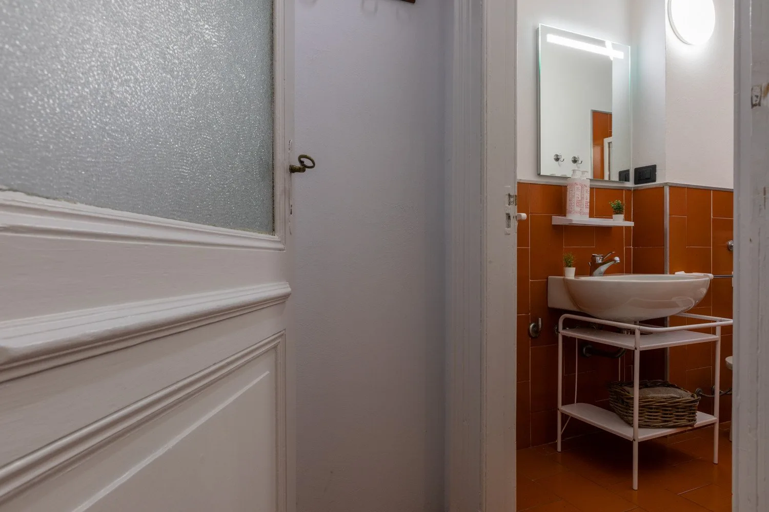 A bathroom vanity with a basin, mirror, and orange wall tiles.