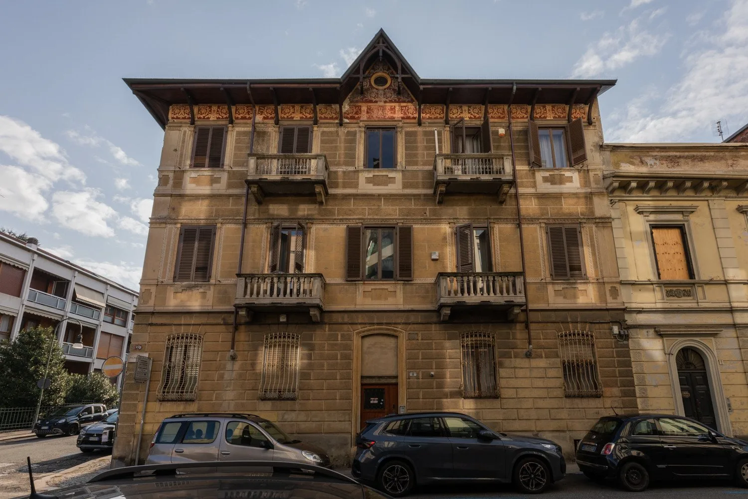 A multi-story stone building with balconies stands along a city street.