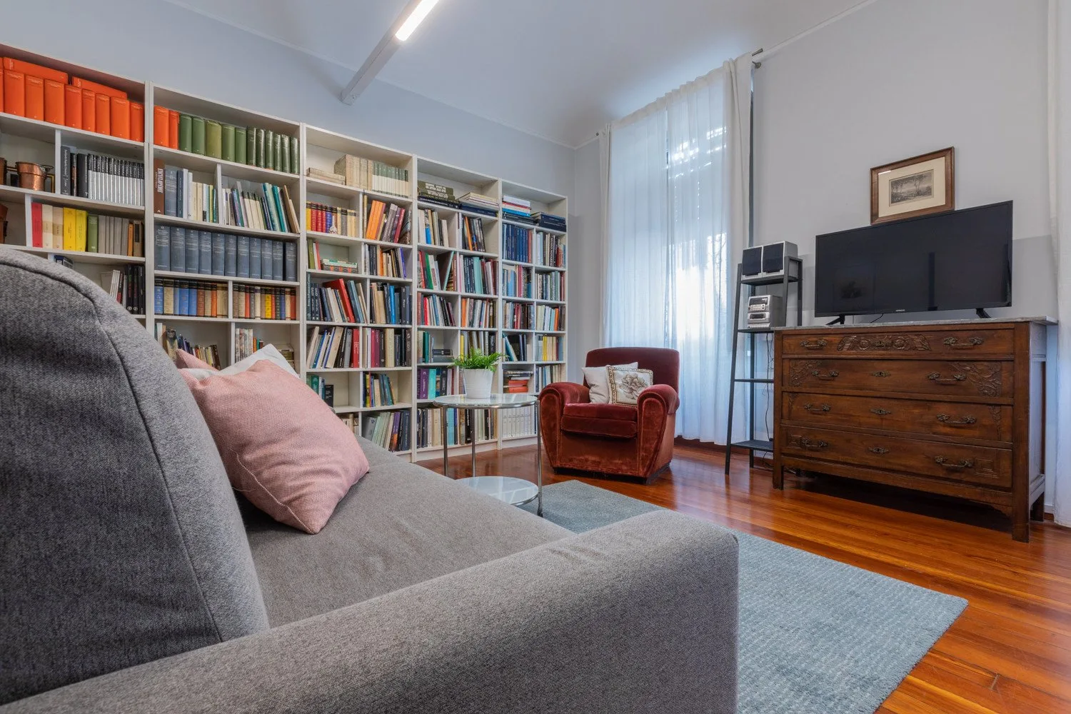 A living room with bookshelves, seating, and a television on a wooden dresser.