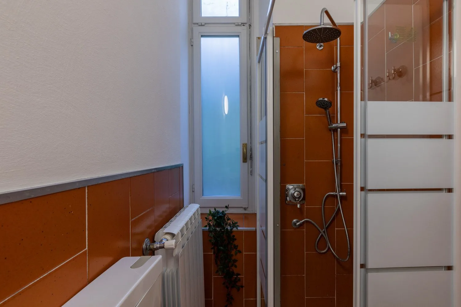 A narrow bathroom with a shower, tiled walls, and a frosted window.