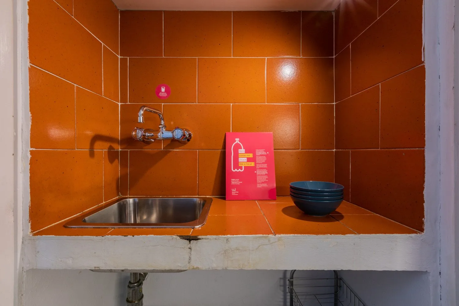 A tiled wash area with a small sink, wall-mounted faucet, and bowl.