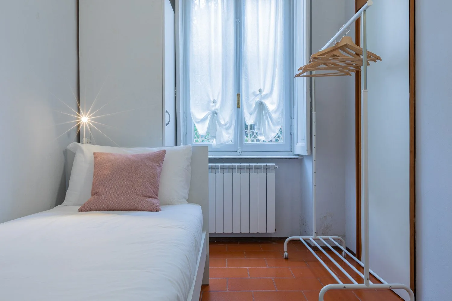 A bedroom with a single bed, curtained window, and clothing rack.