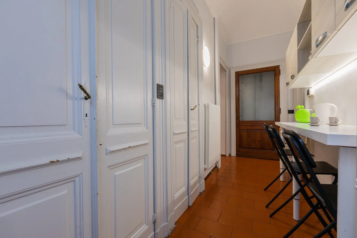 A narrow kitchen area with a counter and stools beside a hallway.