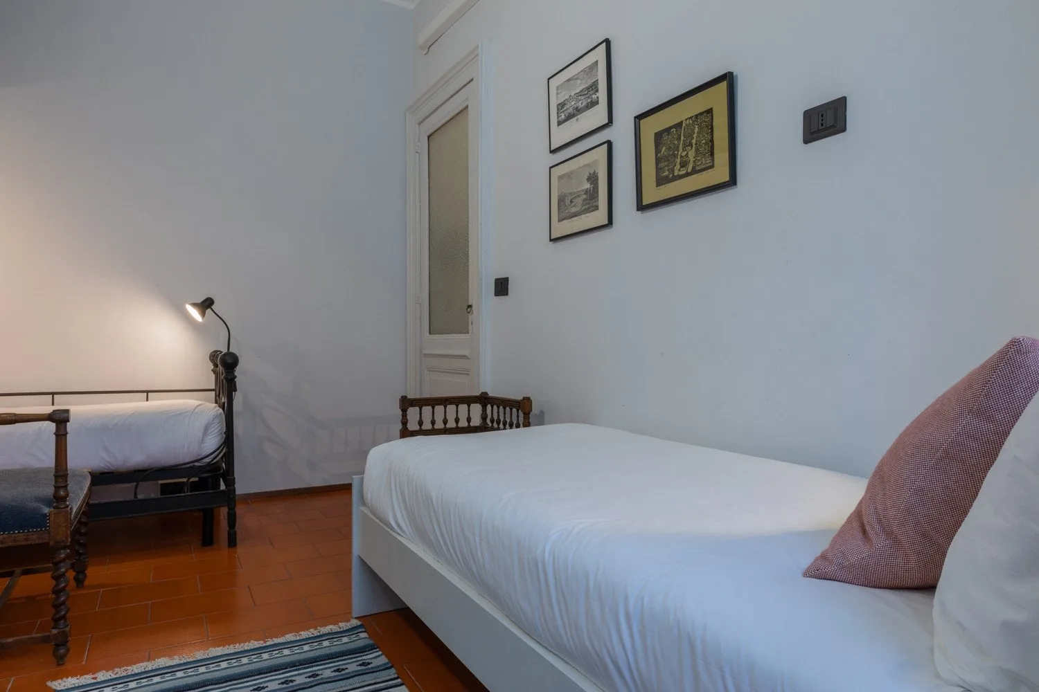 A bedroom with two beds, framed pictures, and a bedside lamp.