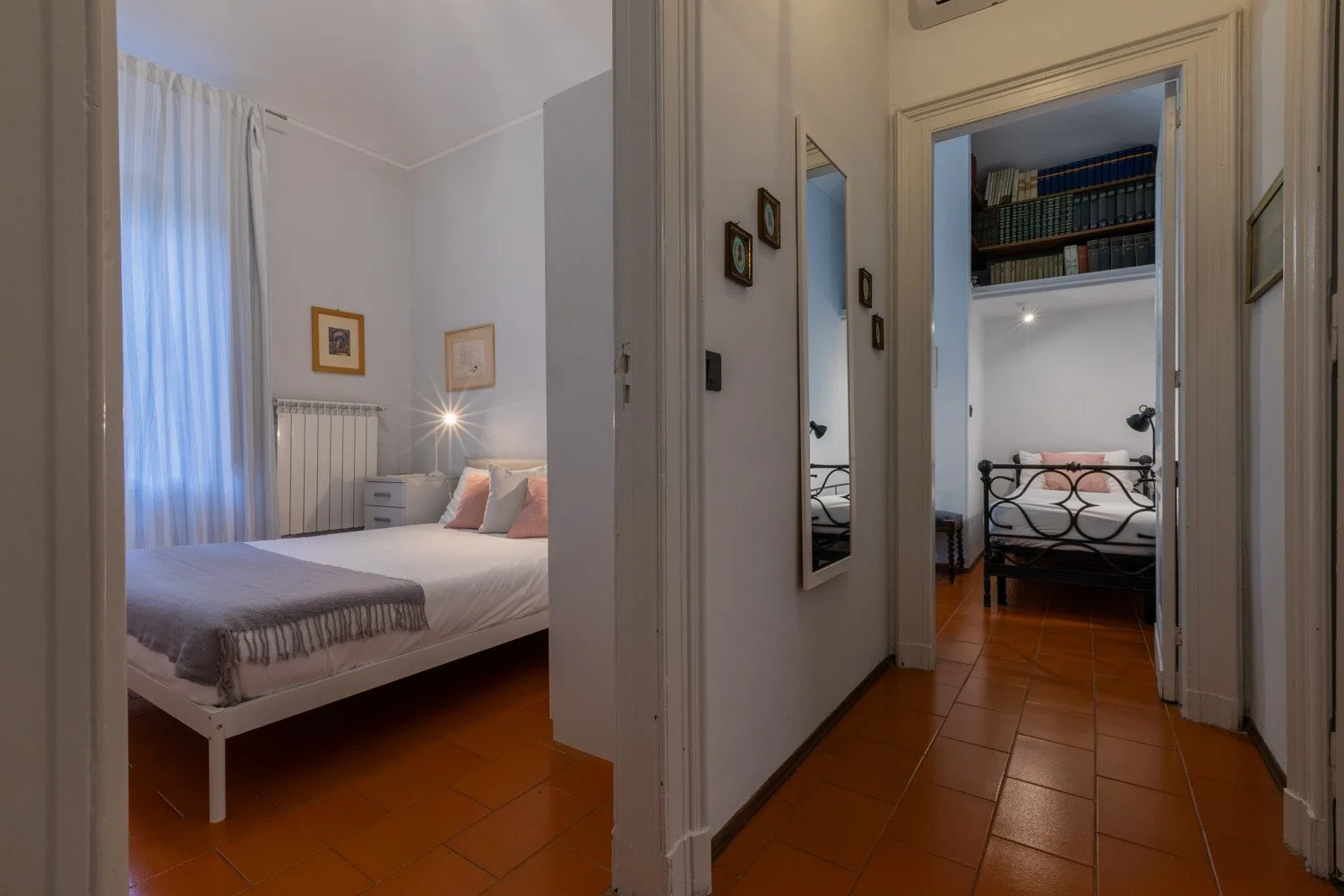 A hallway opens onto two bedrooms, with beds and terracotta-colored tile floors visible.