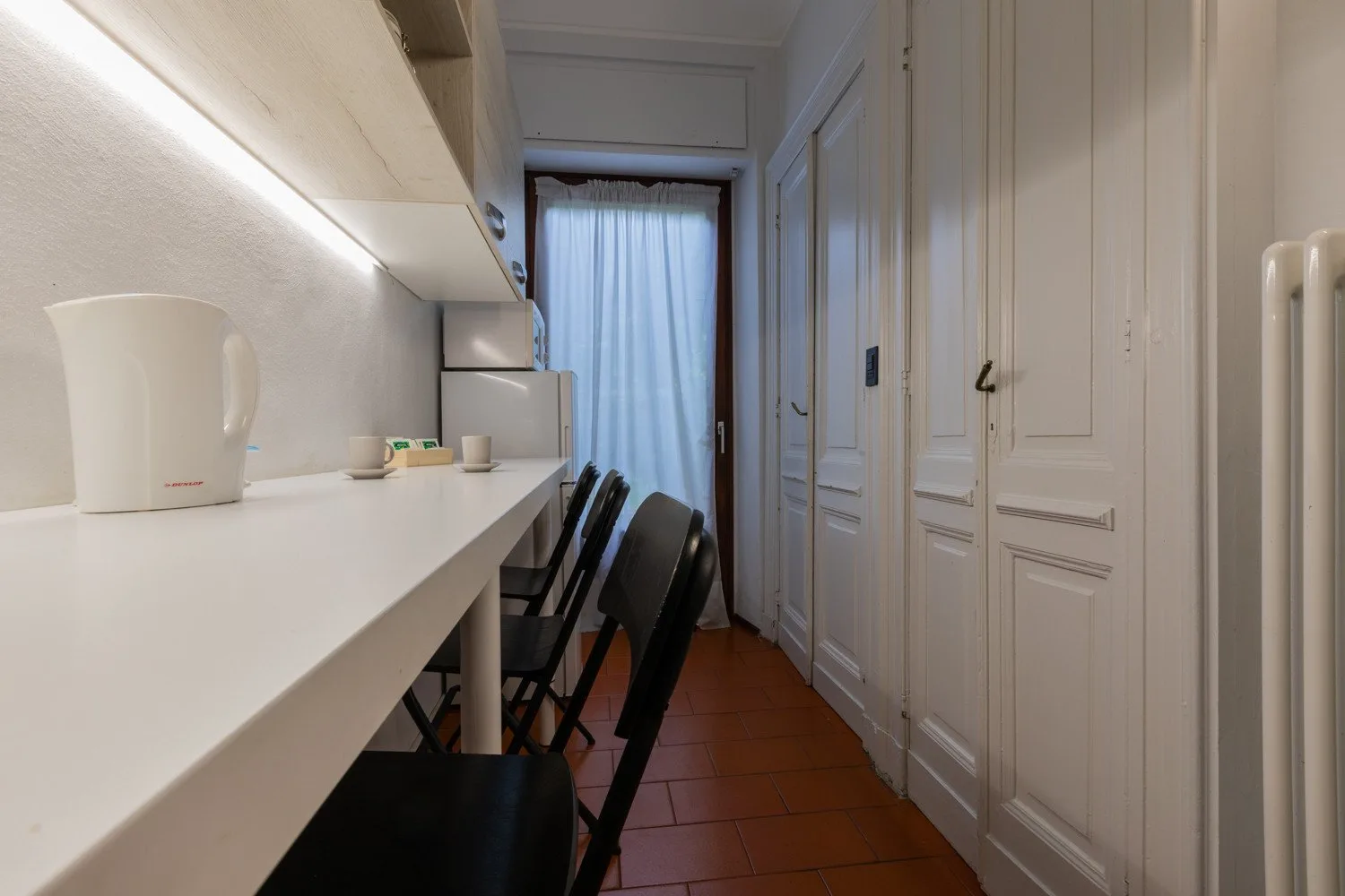 A narrow dining area with a counter, seating, and a curtained window.