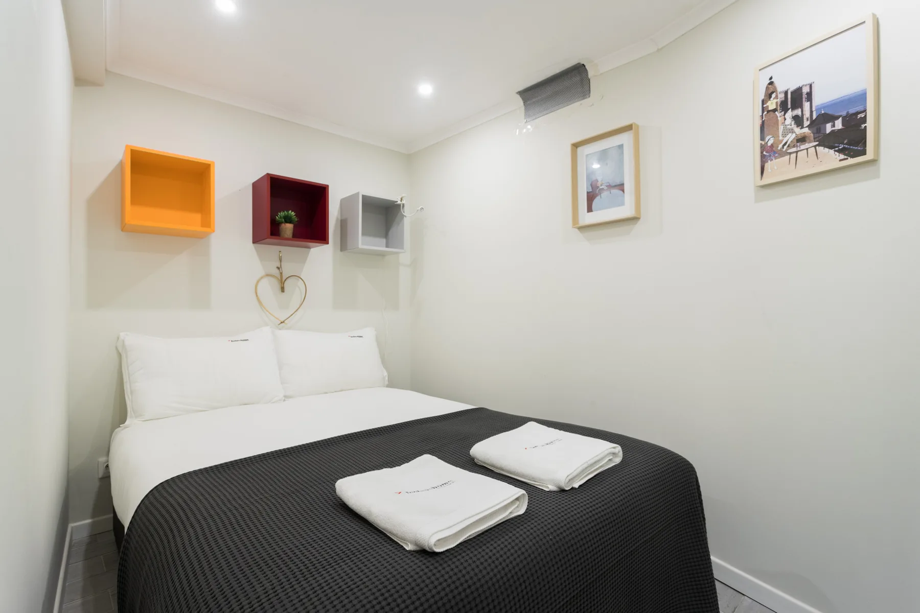 A bedroom with a neatly made bed and colorful wall shelves.