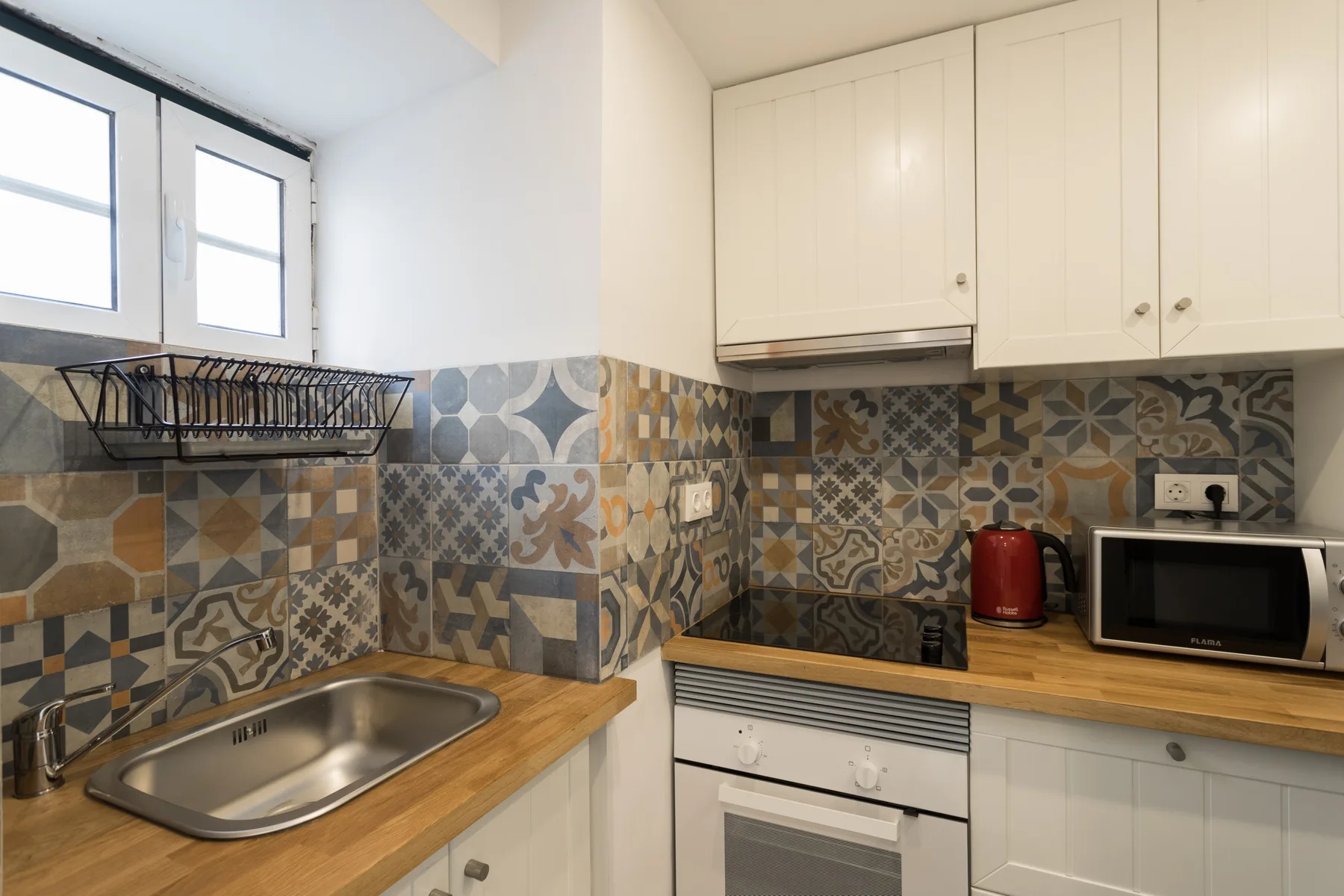 A bright kitchen with patterned tile, wood counters, and a stainless-steel sink.